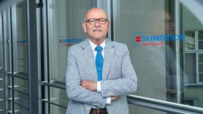 Porträt Rolf Rosenbrock vor Glastür mit dem Logo des Paritätischen Wohlfahrtsverbands