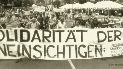 schwarz-weißes Demo-Foto mit Banner "Solidarität der Uneinsichtigen"